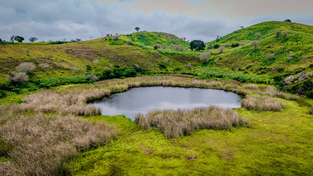 Aerial view of a serene pond surrounded by lush green hills tall grasses and rocky terrain in Mangu Plateau Nigeria. Aerial view of a serene pond surrounded by lush green hills tall grasses and rocky terrain in Mangu Plateau Nigeria.