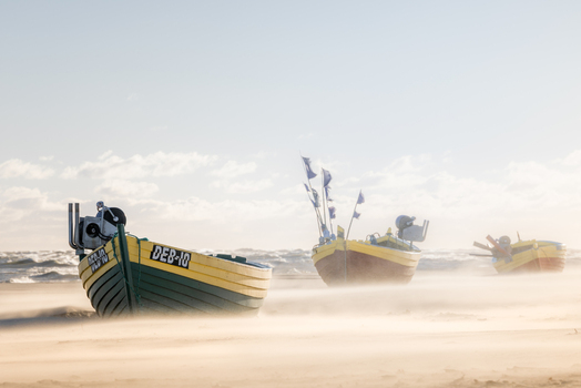 View of traditional fishing boats resting on a sandy beach with windblown sand and a choppy sea under a bright sky in Debki Pomeranian Voivodeship Poland. View of traditional fishing boats resting on a sandy beach with windblown sand and a choppy sea under a bright sky in Debki Pomeranian Voivodeship Poland.