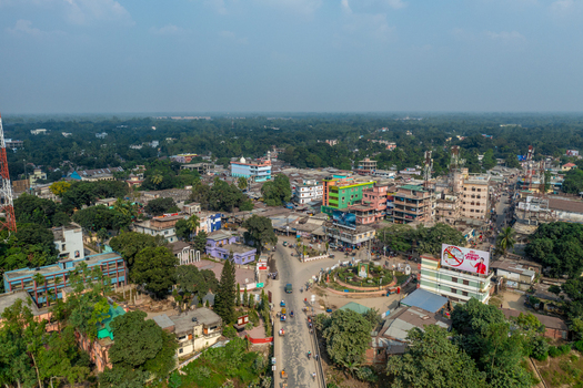 Aerial view of the town of Panchagarh featuring a central roundabout dense urban buildings and lush green trees under a clear sky in Panchagarh Rangpur Division Bangladesh. Aerial view of the town of Panchagarh featuring a central roundabout dense urban buildings and lush green trees under a clear sky in Panchagarh Rangpur Division Bangladesh.