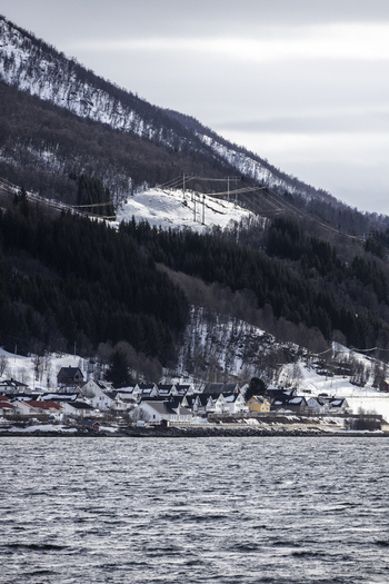View of traditional houses along the coastline at the foot of a snow covered mountain under an overcast sky Tromso Troms Norway.