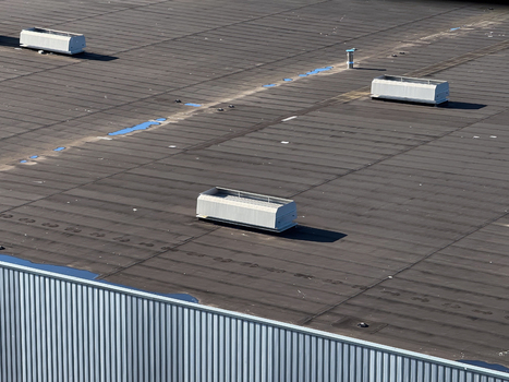 Aerial view of a flat industrial building roof featuring several white ventilation units and small puddles of water in Leeuwarden Friesland Netherlands.