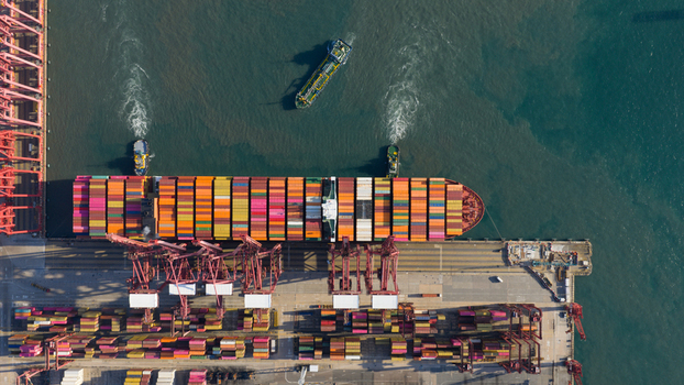 Aerial view of a large cargo ship loaded with colorful containers docked at a busy port terminal with red gantry cranes and tugboats Hong Kong Hong Kong. Aerial view of a large cargo ship loaded with colorful containers docked at a busy port terminal with red gantry cranes and tugboats Hong Kong Hong Kong.