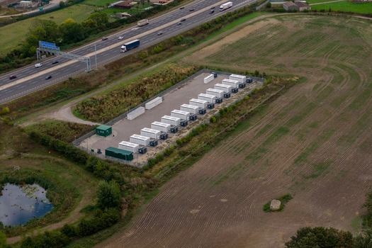 Aerial view of Chapel Farm Energy Park featuring rows of white battery storage containers and electrical equipment situated in a rural field near a highway in Luton England United Kingdom. Aerial view of Chapel Farm Energy Park featuring rows of white battery storage containers and electrical equipment situated in a rural field near a highway in Luton England United Kingdom.