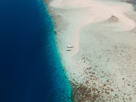 Aerial view of Pasir Timbul Mansuar sandbar surrounded by shallow turquoise water and deep blue sea with two small boats anchored in Raja Ampat Papua Barat Indonesia. Aerial view of Pasir Timbul Mansuar sandbar surrounded by shallow turquoise water and deep blue sea with two small boats anchored in Raja Ampat Papua Barat Indonesia.