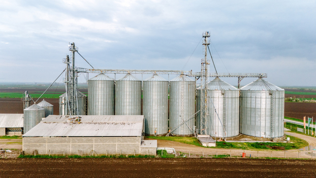 Aerial view of towering silver grain silos gleaming under a cloudy sky standing stark against the brown earth Sremska Mitrovica Vojvodina Serbia. Aerial view of towering silver grain silos gleaming under a cloudy sky standing stark against the brown earth Sremska Mitrovica Vojvodina Serbia.