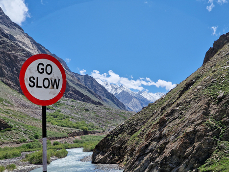 View of a GO SLOW road sign along the Penzi La road with a river flowing through a rocky mountain valley in Zanskar Ladakh India.