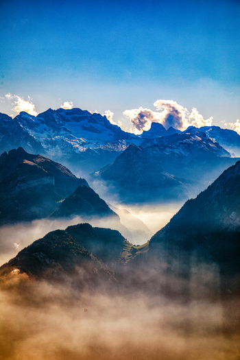 Aerial view of Swiss Alps with dramatic mountain peaks rising above a thick layer of morning mist under a clear blue sky Airolo Ticino Switzerland. Aerial view of Swiss Alps with dramatic mountain peaks rising above a thick layer of morning mist under a clear blue sky Airolo Ticino Switzerland.