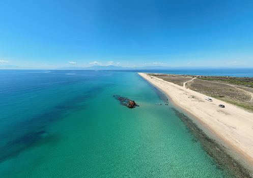 Aerial view of the Shipwreck Epanomi with its rusted hull resting in turquoise waters along a sandy beach under a clear blue sky in Epanomi Greece.