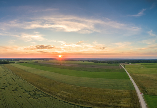 Aerial view of a vast rural landscape with green agricultural fields a dirt road and a vibrant sunset sky in Latvia. Aerial view of a vast rural landscape with green agricultural fields a dirt road and a vibrant sunset sky in Latvia.