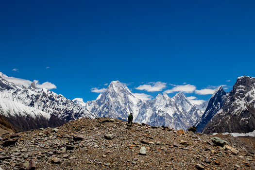 View of a lone hiker standing on a rocky ridge overlooking the snow covered peaks of Gasherbrum IV under a clear blue sky in Skardu Gilgit Pakistan. View of a lone hiker standing on a rocky ridge overlooking the snow covered peaks of Gasherbrum IV under a clear blue sky in Skardu Gilgit Pakistan.