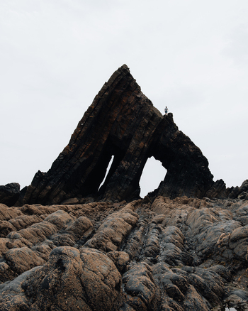 Westward Ho United Kingdom 23 July 2021 View of Blackchurch Rock on the coast with a person standing on top of the jagged dark rock formation under an overcast sky.