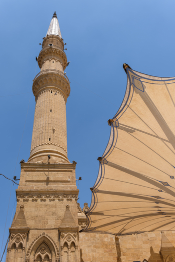 View of the tall stone minaret of the Imam Al Hussein Mosque and a large architectural canopy under a clear blue sky in Cairo Egypt. View of the tall stone minaret of the Imam Al Hussein Mosque and a large architectural canopy under a clear blue sky in Cairo Egypt.