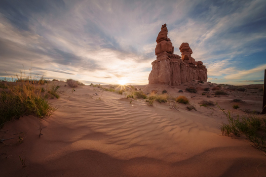 View of warm sunlight kisses the surreal undulating red rock formations and sandy dunes under a painted sky Green River Utah United States.