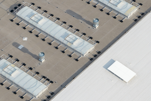 Aerial view of a flat industrial roof featuring multiple skylights ventilation units and a white section in Poland. Aerial view of a flat industrial roof featuring multiple skylights ventilation units and a white section in Poland.