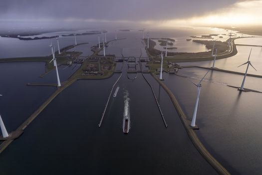 Aerial view of the Krammer locks featuring a cargo ship navigating the waterway surrounded by wind turbines under a dramatic sky in Bruinisse Zeeland Netherlands. Aerial view of the Krammer locks featuring a cargo ship navigating the waterway surrounded by wind turbines under a dramatic sky in Bruinisse Zeeland Netherlands.