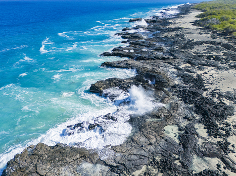 Aerial view of the rugged Kalaemamo coastline featuring black volcanic rocks and crashing white waves against turquoise water in Hawaii County Hawaii United States. Aerial view of the rugged Kalaemamo coastline featuring black volcanic rocks and crashing white waves against turquoise water in Hawaii County Hawaii United States.