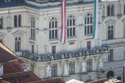 View of ornate architecture adorned with Austrian and Styrian flags casting shadows on sculpted figures below a blend of history and culture Graz Styria Austria. View of ornate architecture adorned with Austrian and Styrian flags casting shadows on sculpted figures below a blend of history and culture Graz Styria Austria.