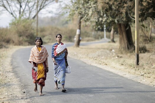 Odisha India 26 March 2026 View of two women walking along a sun drenched road their colorful saris contrasting with the dry muted tones of the landscape. Odisha India 26 March 2026 View of two women walking along a sun drenched road their colorful saris contrasting with the dry muted tones of the landscape.
