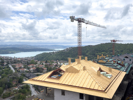 View of a house under construction with a wooden roof frame and tall cranes overlooking the Bosphorus and green hills in Sariyer Istanbul Turkiye.