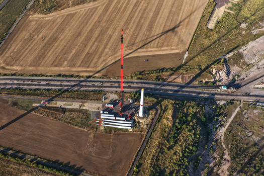 Aerial view of a wind turbine construction site with a tall red crane turbine blades and a tower base near the Schleenhain lignite open cast mine in Zwenkau Saxony Germany.