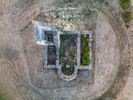 Aerial view of the medieval church ruins in Csabdi Hungary showing exposed stone foundations an apsidal end grave markers and dry grass around the historic site.
