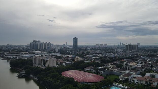 Aerial view of the urban skyline with high rise buildings residential neighborhoods and a prominent red roofed structure situated near the water in North Jakarta Jakarta Indonesia. Aerial view of the urban skyline with high rise buildings residential neighborhoods and a prominent red roofed structure situated near the water in North Jakarta Jakarta Indonesia.