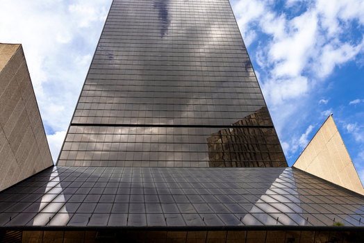 View of a towering modern glass skyscraper reflecting white clouds under a bright blue sky flanked by angular concrete structures in Mexico City Mexico City Mexico. View of a towering modern glass skyscraper reflecting white clouds under a bright blue sky flanked by angular concrete structures in Mexico City Mexico City Mexico.