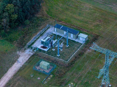 Aerial view of a small electrical transformer station with metal fencing green cabinets and a nearby high voltage power pylon in a rural field in Jacobsdorf Brandenburg Germany. Aerial view of a small electrical transformer station with metal fencing green cabinets and a nearby high voltage power pylon in a rural field in Jacobsdorf Brandenburg Germany.