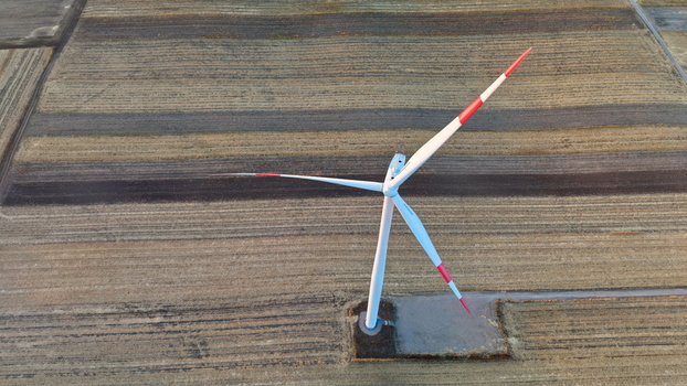 Aerial view of a wind turbine with red tipped blades standing in a vast agricultural field in Vladimirovac Vojvodina Serbia.