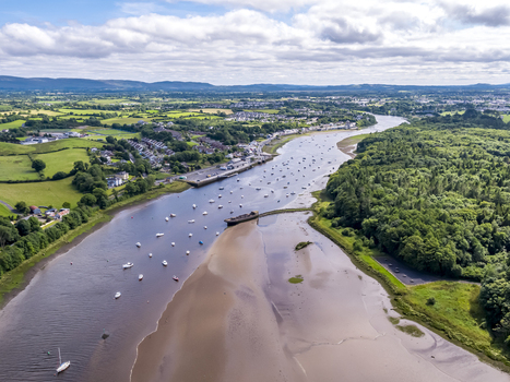 Aerial view of the River Moy flowing through the town with boats moored in the water surrounded by lush green fields and woodlands under a cloudy sky in Ballina County Mayo Ireland.