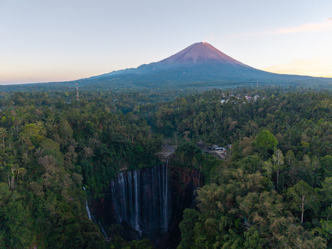 Aerial view of Tumpak Sewu Waterfall with the majestic Mount Semeru in the background surrounded by lush tropical rainforest in Kecamatan Pronojiwo Jawa Timur Indonesia.