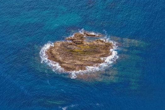 Aerial view of a rocky islet surrounded by crashing waves and deep blue sea in Cudillero Asturias Spain.