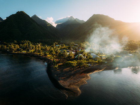 Aerial view of the lush tropical coastline and jagged volcanic mountains with smoke rising from a village at sunset in Moorea Maiao Windward Islands French Polynesia. Aerial view of the lush tropical coastline and jagged volcanic mountains with smoke rising from a village at sunset in Moorea Maiao Windward Islands French Polynesia.