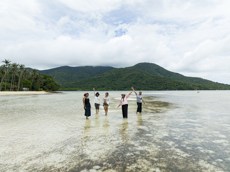 Aerial view of people wading in the shallow clear waters of Bobby Beach with lush green hills rising in the background Karimunjawa Central Java Indonesia.