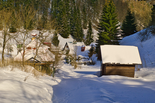 View of rustic wooden huts nestled amidst a snow covered landscape with tall evergreens casting long shadows in Moce Banska Bystrica Region Slovakia.