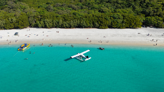 Aerial view of Whitehaven Beach with a seaplane anchored in turquoise water white sand lush forest and people enjoying the beach in Whitsundays Queensland Australia.