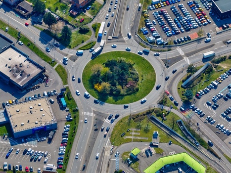 Aerial view of a vibrant roundabout where vehicles weave around a lush green island under the bright sky Sausheim Grand Est France.