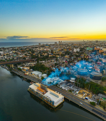 Aerial view of the Seaboard Transcontinental power plant on the Ozama River with industrial structures smoke and the urban landscape of Santo Domingo Distrito Nacional Dominican Republic. Aerial view of the Seaboard Transcontinental power plant on the Ozama River with industrial structures smoke and the urban landscape of Santo Domingo Distrito Nacional Dominican Republic.