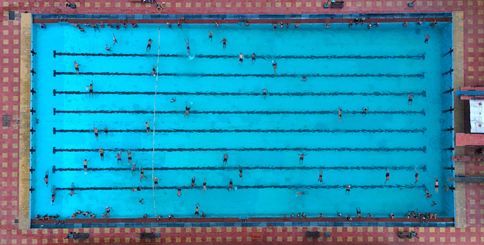 Aerial view of a large rectangular swimming pool with many people swimming in lanes surrounded by a red and yellow tiled deck in Surat Gujarat India. Aerial view of a large rectangular swimming pool with many people swimming in lanes surrounded by a red and yellow tiled deck in Surat Gujarat India.