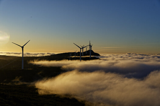 Aerial view of wind turbines at Bica da Cana peak rising above a thick sea of clouds during golden hour in Funchal Madeira Portugal.