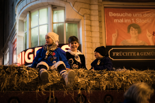 Basel Switzerland 10 March 2025 View of children in traditional costumes atop a hay covered float their bright outfits a stark contrast to the dimly lit street during Fasnacht. Basel Switzerland 10 March 2025 View of children in traditional costumes atop a hay covered float their bright outfits a stark contrast to the dimly lit street during Fasnacht.