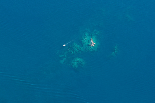 Aerial view of a small motorboat navigating near the rocky outcrops of Le Trayas in the deep blue waters of the Mediterranean Sea Saint Raphael Provence Alpes Cote d Azur France. Aerial view of a small motorboat navigating near the rocky outcrops of Le Trayas in the deep blue waters of the Mediterranean Sea Saint Raphael Provence Alpes Cote d Azur France.