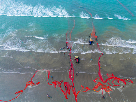 Cox s Bazar Bangladesh 10 March 2026 Aerial view of the beach with vibrant red patterns contrasting against the turquoise sea and sandy shore near fishing boats and tractors.