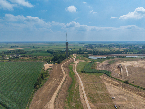 Aerial view of a tall communication tower standing amidst rural fields dirt paths and a small pond under a blue sky in the Netherlands. Aerial view of a tall communication tower standing amidst rural fields dirt paths and a small pond under a blue sky in the Netherlands.