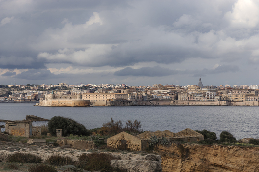 View of Maniace Castle and the historic skyline of Ortigia across the sea under a dramatic cloudy sky Syracuse Sicily Italy.