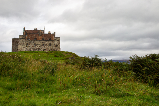 View of Duart Castle a historic stone fortress standing on a grassy hill under a dramatic overcast sky with lush green vegetation Isle of Mull Scotland United Kingdom.