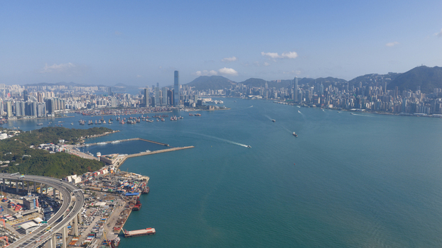 Aerial view of Victoria Harbour with skyscrapers cargo ships and a highway bridge under a clear blue sky in Hong Kong Hong Kong. Aerial view of Victoria Harbour with skyscrapers cargo ships and a highway bridge under a clear blue sky in Hong Kong Hong Kong.