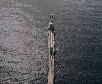Aerial view of a long industrial pier extending into the deep blue sea featuring conveyor structures and machinery in Bajos de Haina San Cristobal Province Dominican Republic.