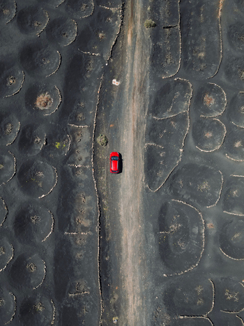 Aerial view of a red car driving on a dirt road through the volcanic landscape of La Geria with circular stone walls for vines in Lanzarote. Aerial view of a red car driving on a dirt road through the volcanic landscape of La Geria with circular stone walls for vines in Lanzarote.