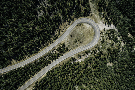 Aerial view of Beartooth Pass featuring a sharp hairpin turn on a winding mountain road surrounded by dense pine forests in Park County Wyoming United States. Aerial view of Beartooth Pass featuring a sharp hairpin turn on a winding mountain road surrounded by dense pine forests in Park County Wyoming United States.